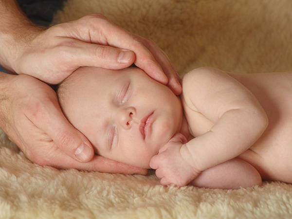 Neugeborenes Baby wird am Kopf gehalten